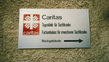 Schild der Caritas-Tagesklinik für Suchtkranke und Fachambulanz für erwachsene Suchtkranke, ca. 1990.  | © (Fotograf unbekannt, Archiv des DiCV München und Freising e. V., Fotosammlung)
