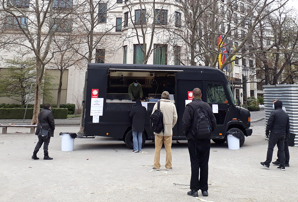 Ein schwarzer Lieferwagen, aus dem Essen ausgegeben wird, steht auf einem Platz.  | © Caritas München und Oberbayern
